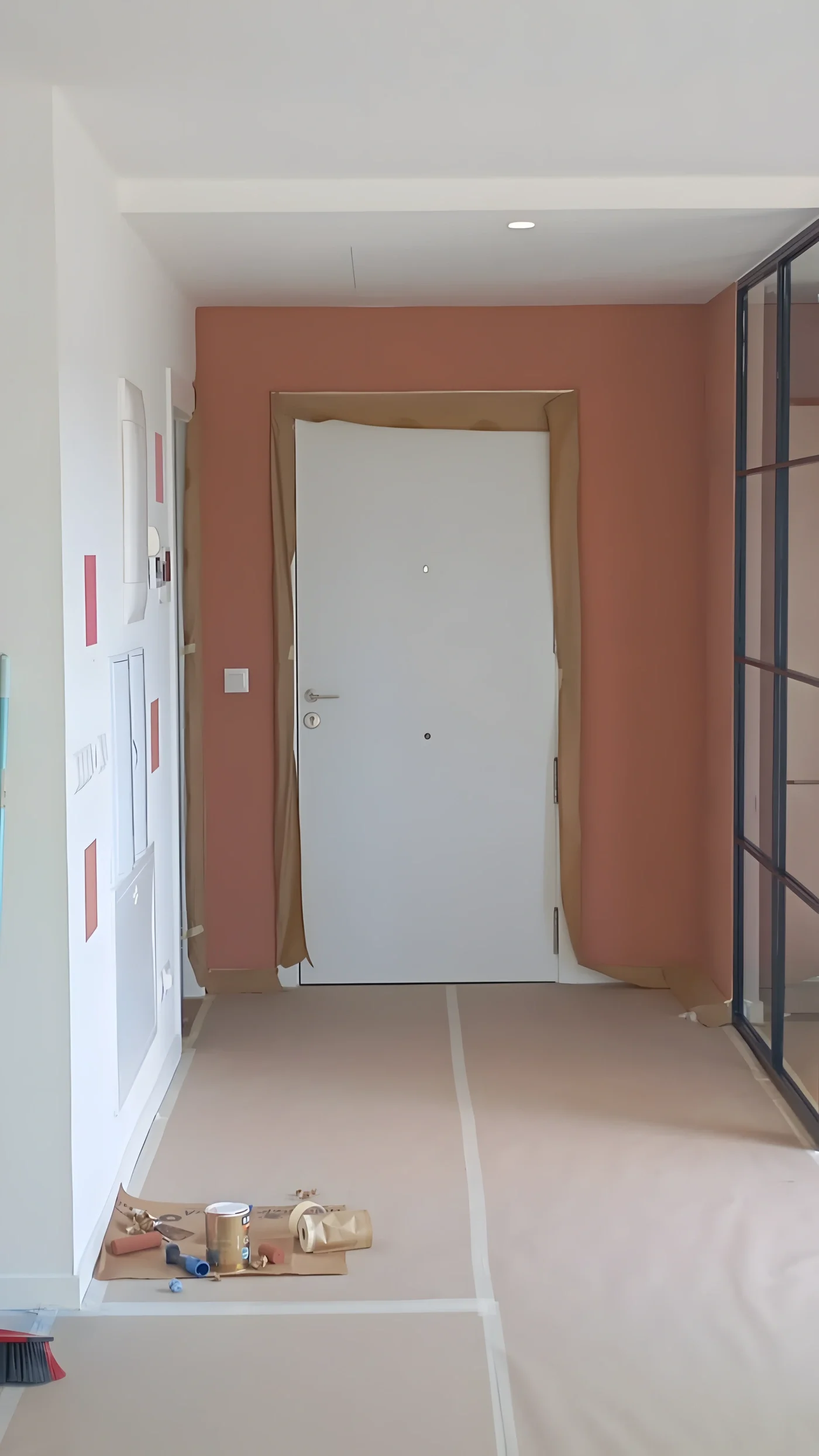 Recibidor con la pared en terracota y la puerta blanca, con el suelo aún protegido