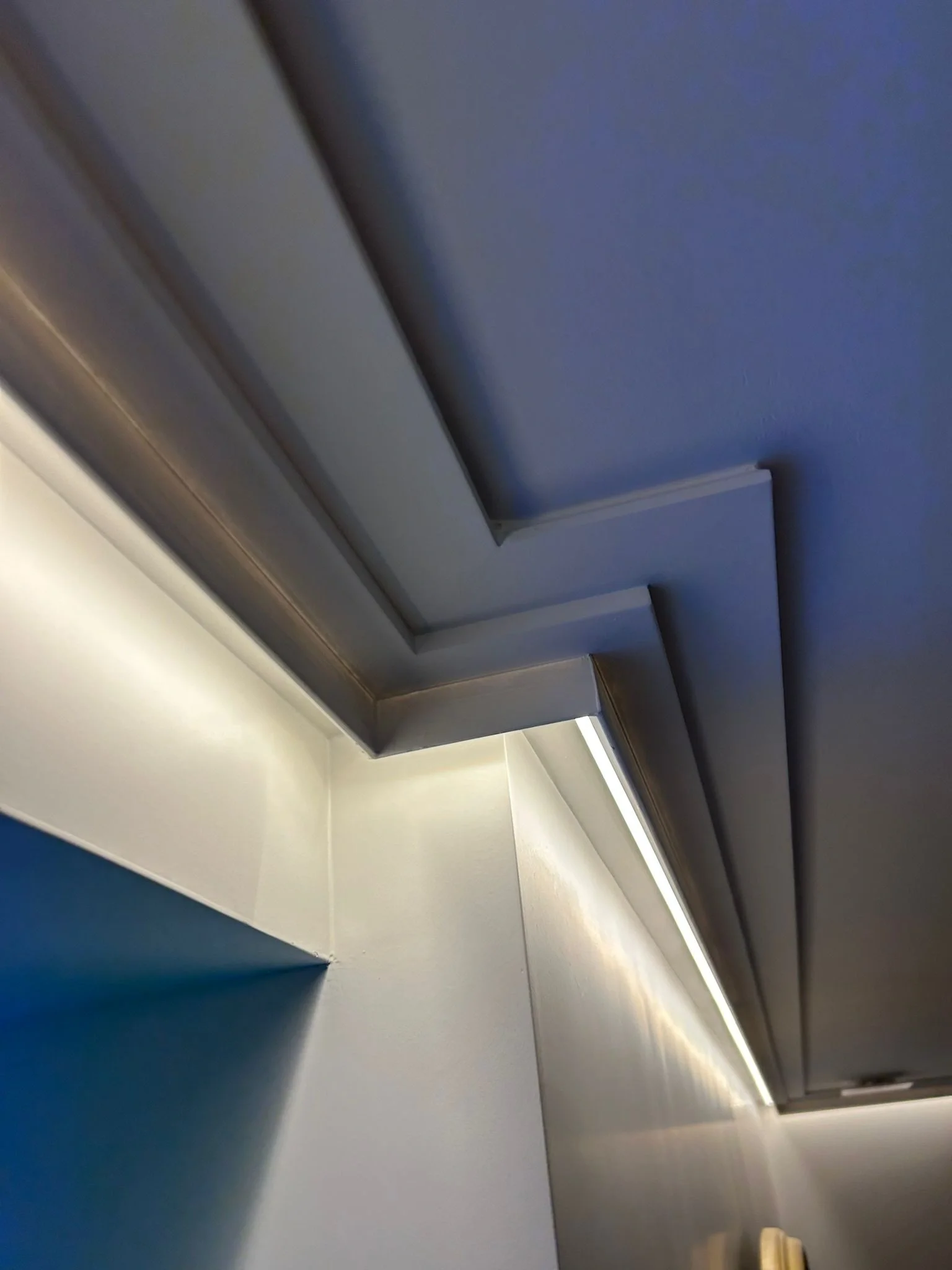 Techo con moldura escalonada e iluminación LED indirecta sobre una pared azul