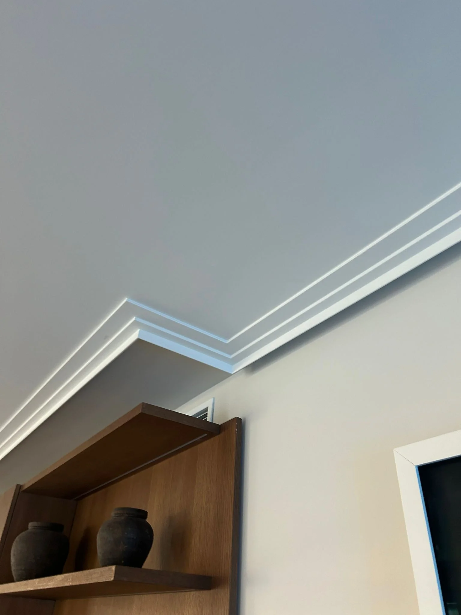 Cornisa blanca en el encuentro de pared y techo, sobre una estantería de madera