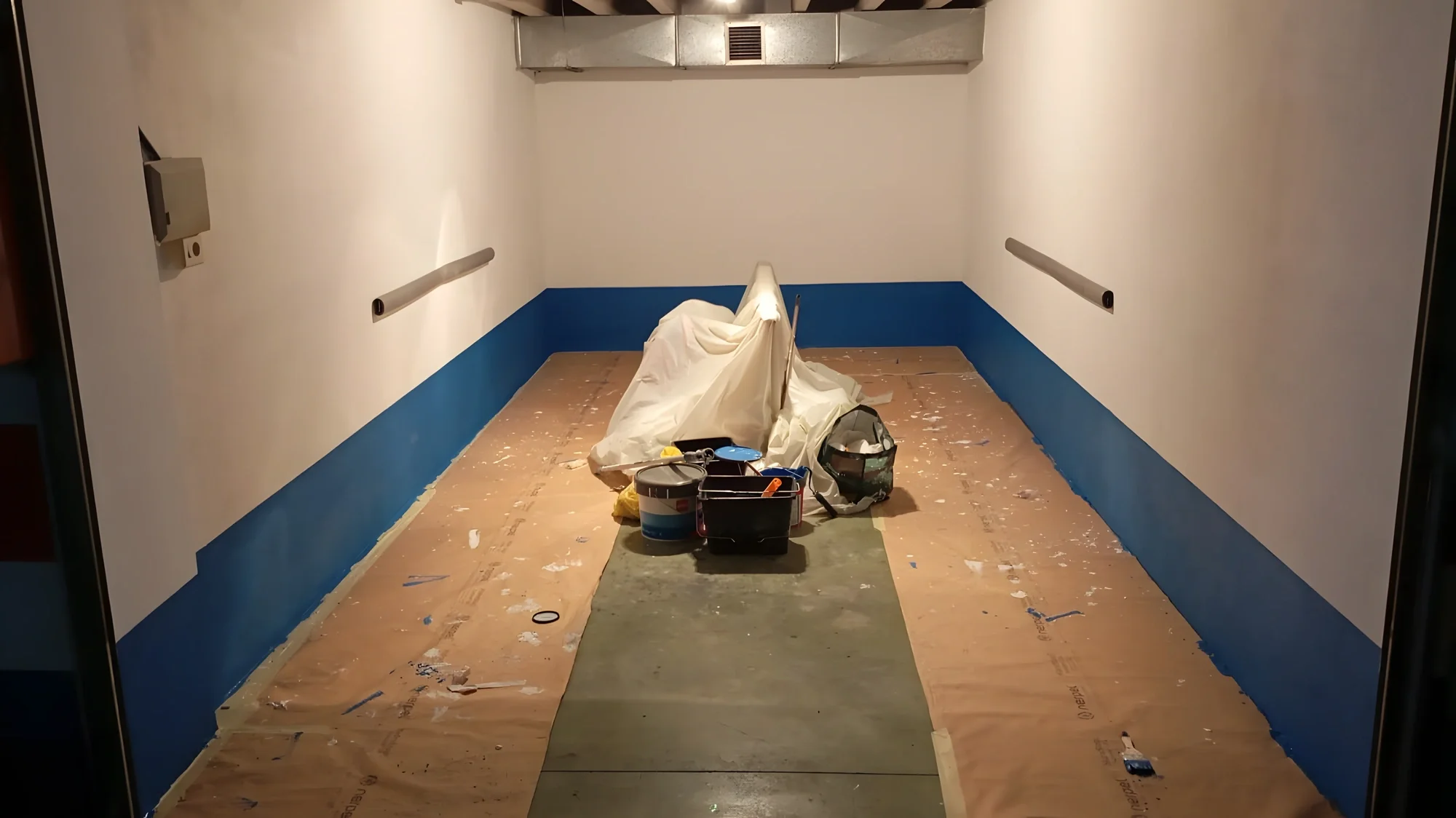 Habitación en obra con el suelo cubierto de papel protector y el zócalo pintado en azul